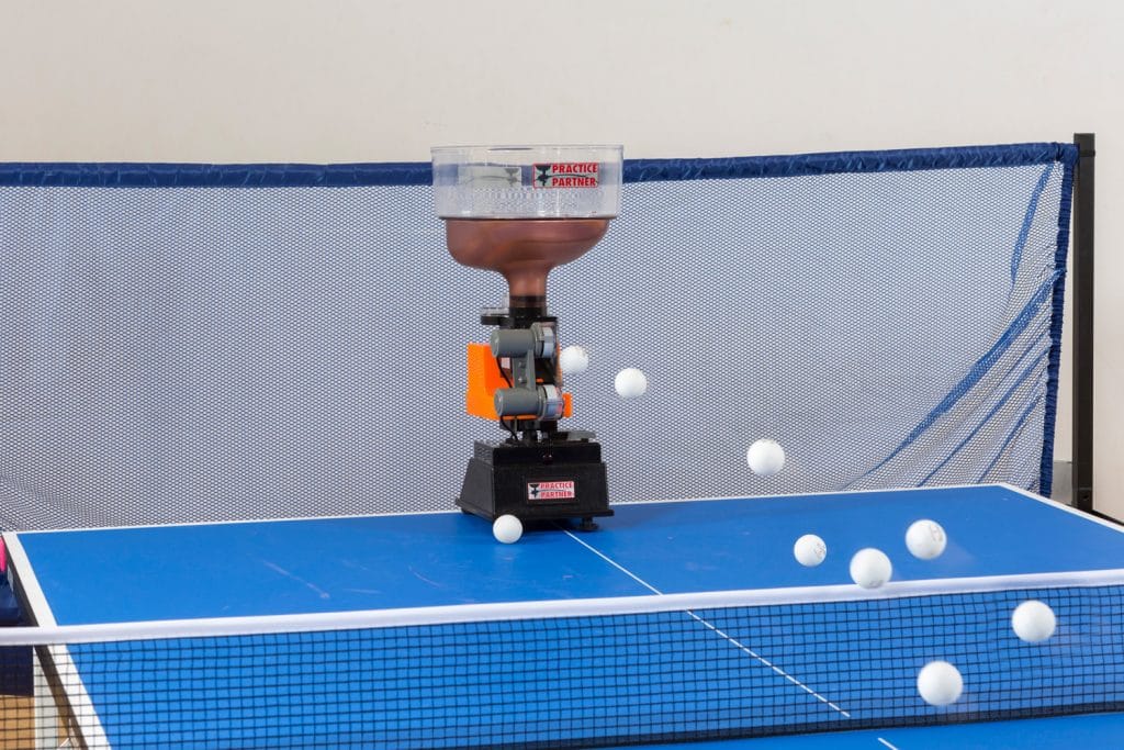 Practice Partner table tennis robot launching white balls on a blue table with net for solo training sessions.